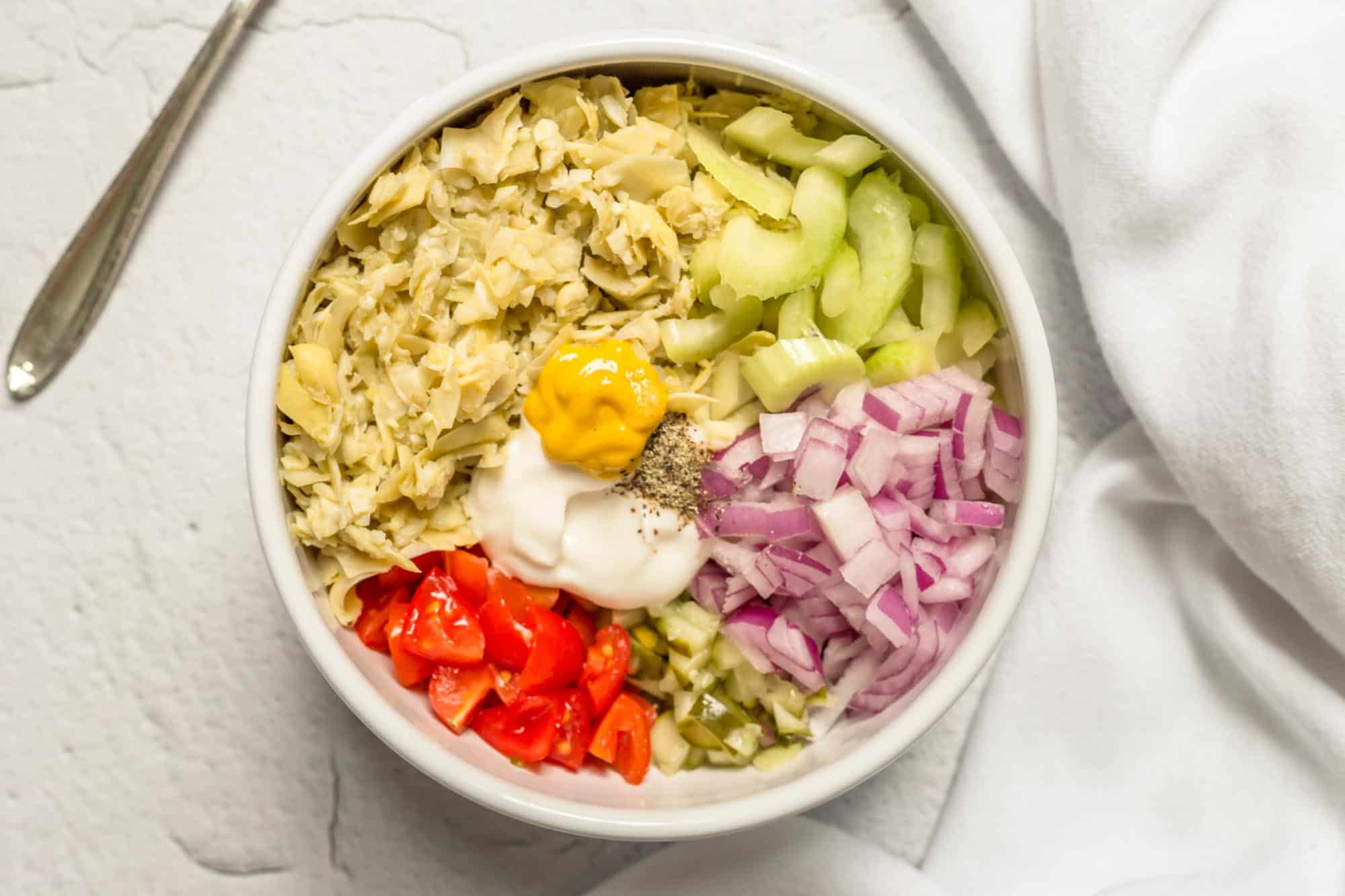 Artichoke Tuna Salad Ingredients in a Bowl Tomatoes Onion Celery Artichoke Hearts Pickes Vegan Mayo Mustard