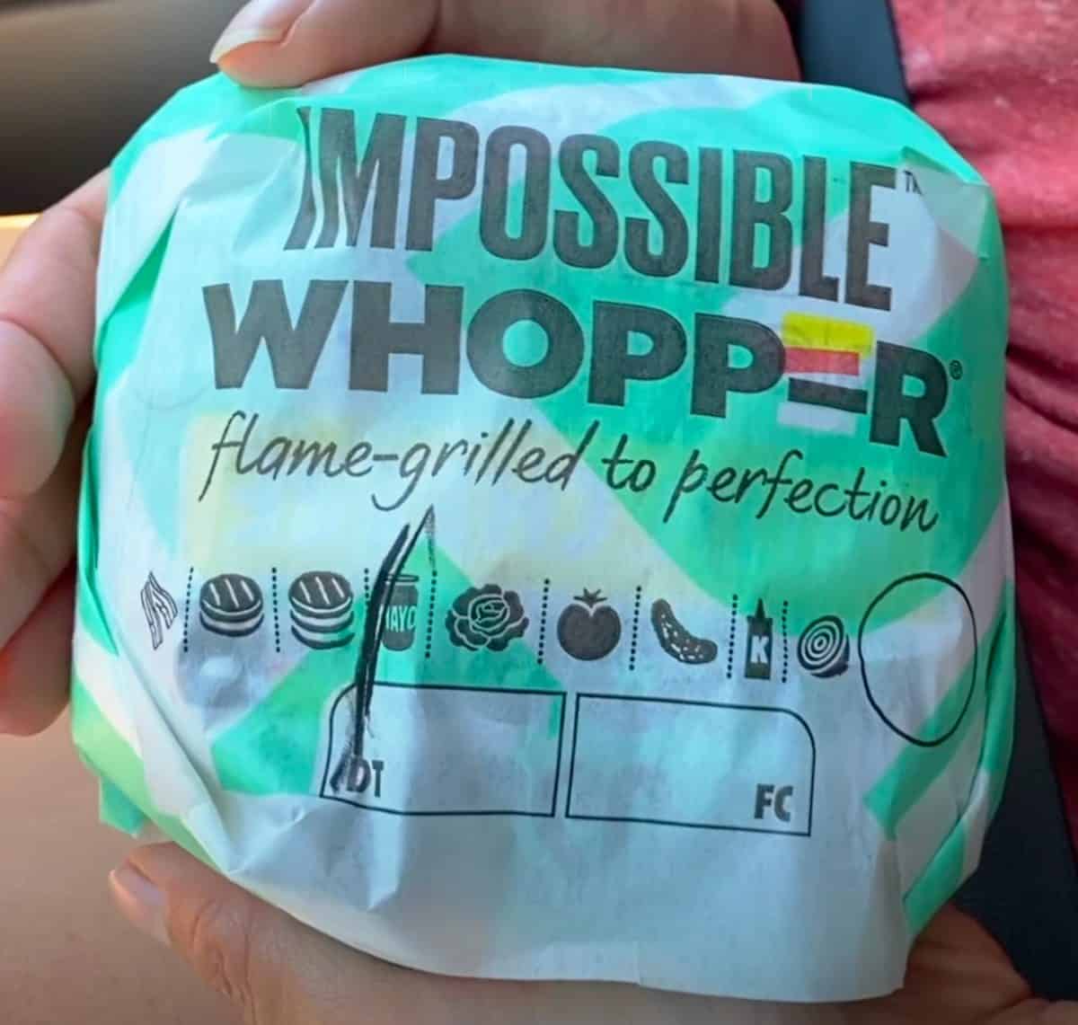 Hands holding an Impossible Whopper in its wrapping.