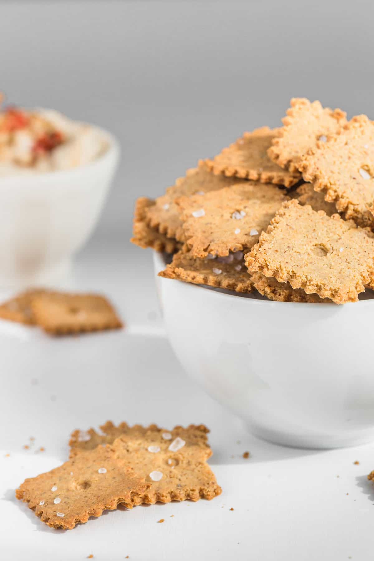 A bowl of almond flour crackers in a white bowl against a white background.