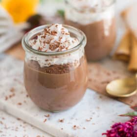 Vegan chocolate pudding in jars, topped with vegan whipped cream and chocolate shavings.