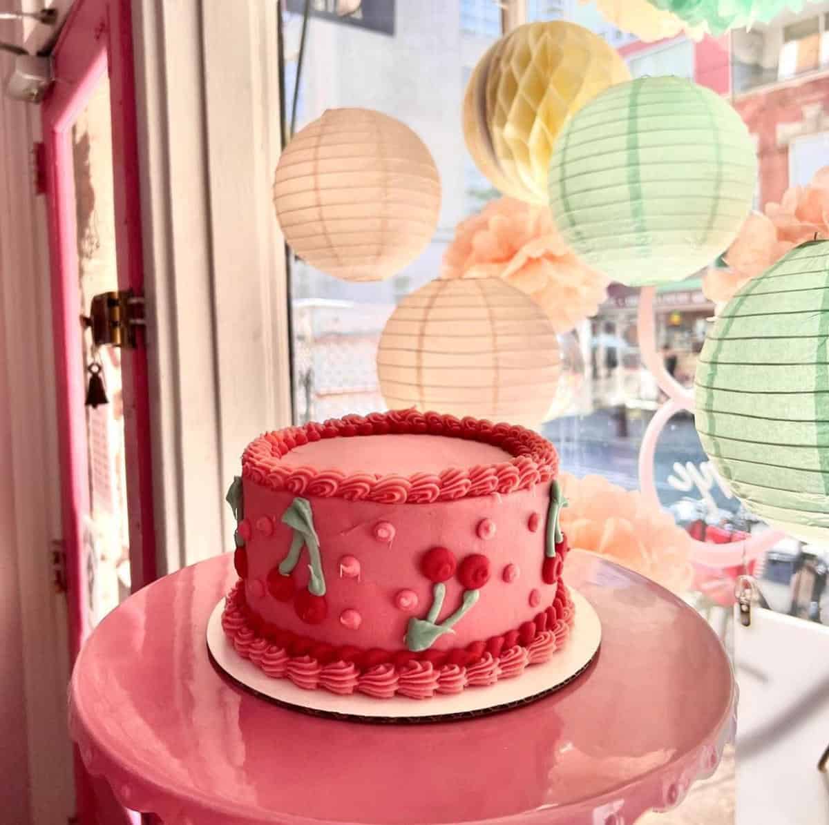 Round vegan cake decorated with cherry theme sitting on a table with lanterns behind it.