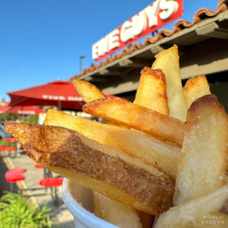 Cup of vegan french fries in front of the Five Guys restaurant sign.