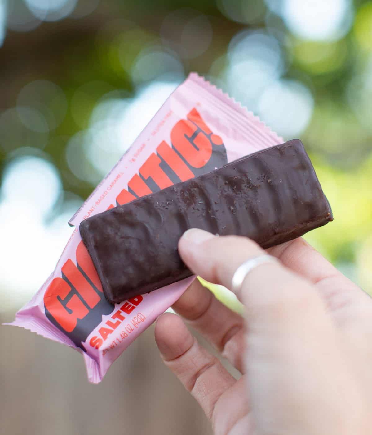 Holding out a plant-based chocolate covered candy bar from Gigantic. 