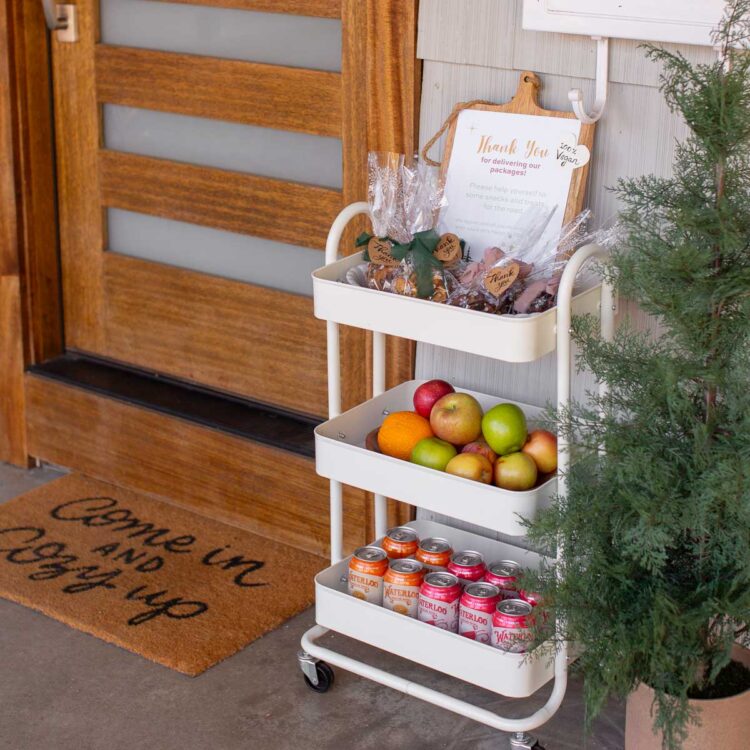 A holiday treat cart filled with vegan cookies, trail mix bags, fruit, and drinks for delivery workers who bring packages.