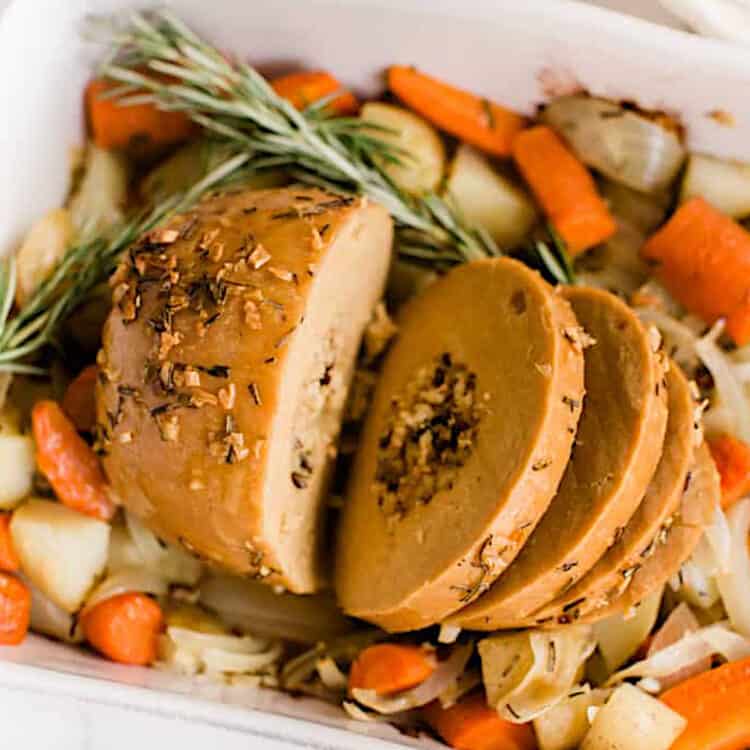 Tofurky roast sliced, in a baking dish on top of roasted vegetables.