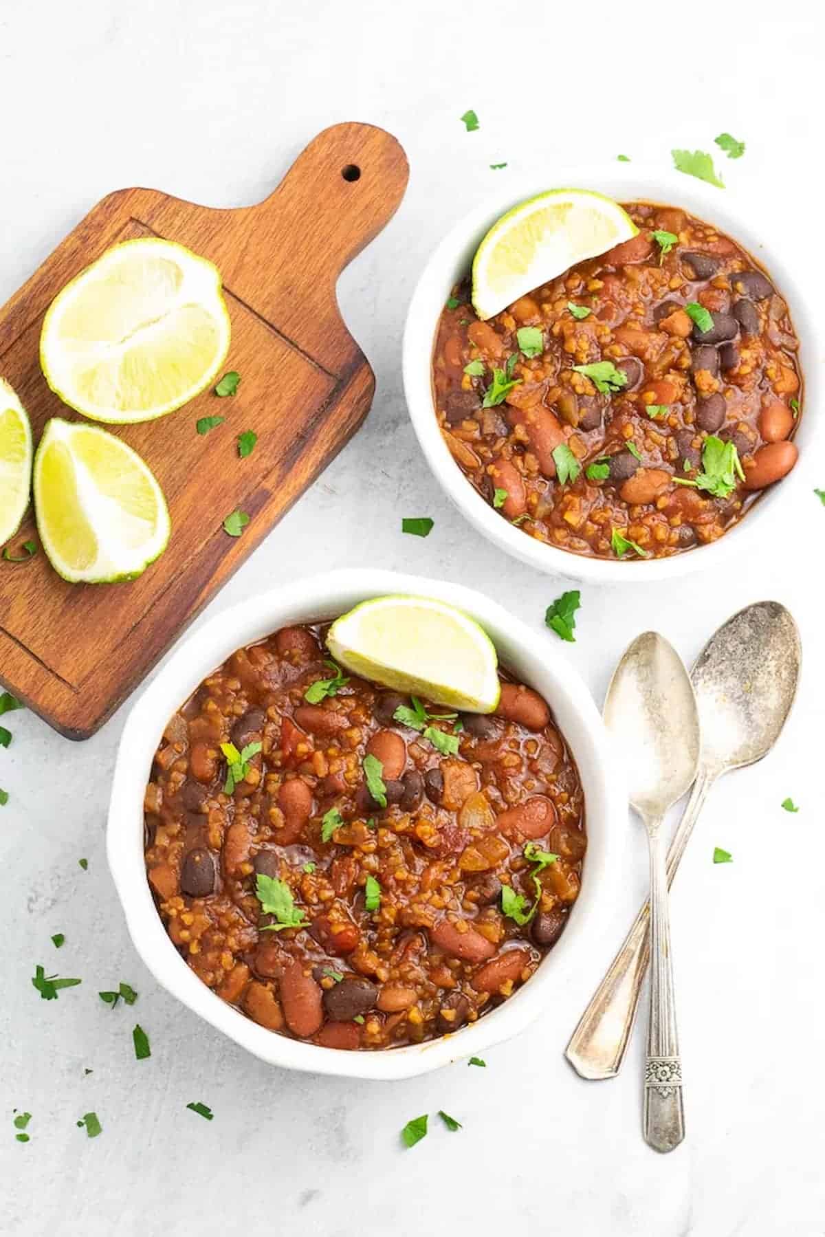Two bowls of vegan chili served with lime wedges with cilantro.