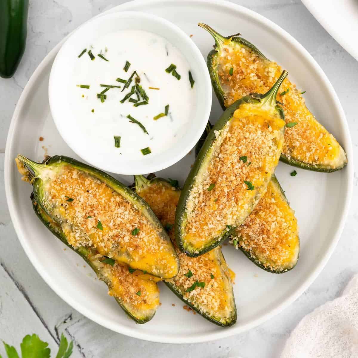 Jalapeno poppers on a white plate, with a small bowl of dip.