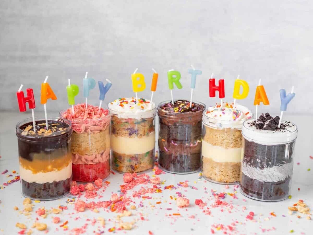 An array of birthday cake cupcakes in mason jars from the online vegan bakery Karma Baker with happy birthday candles.