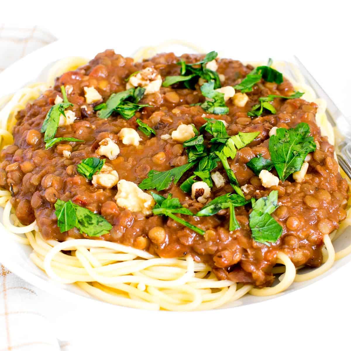A plate of lentil bolognese served over spaghetti and topped with fresh herbs.