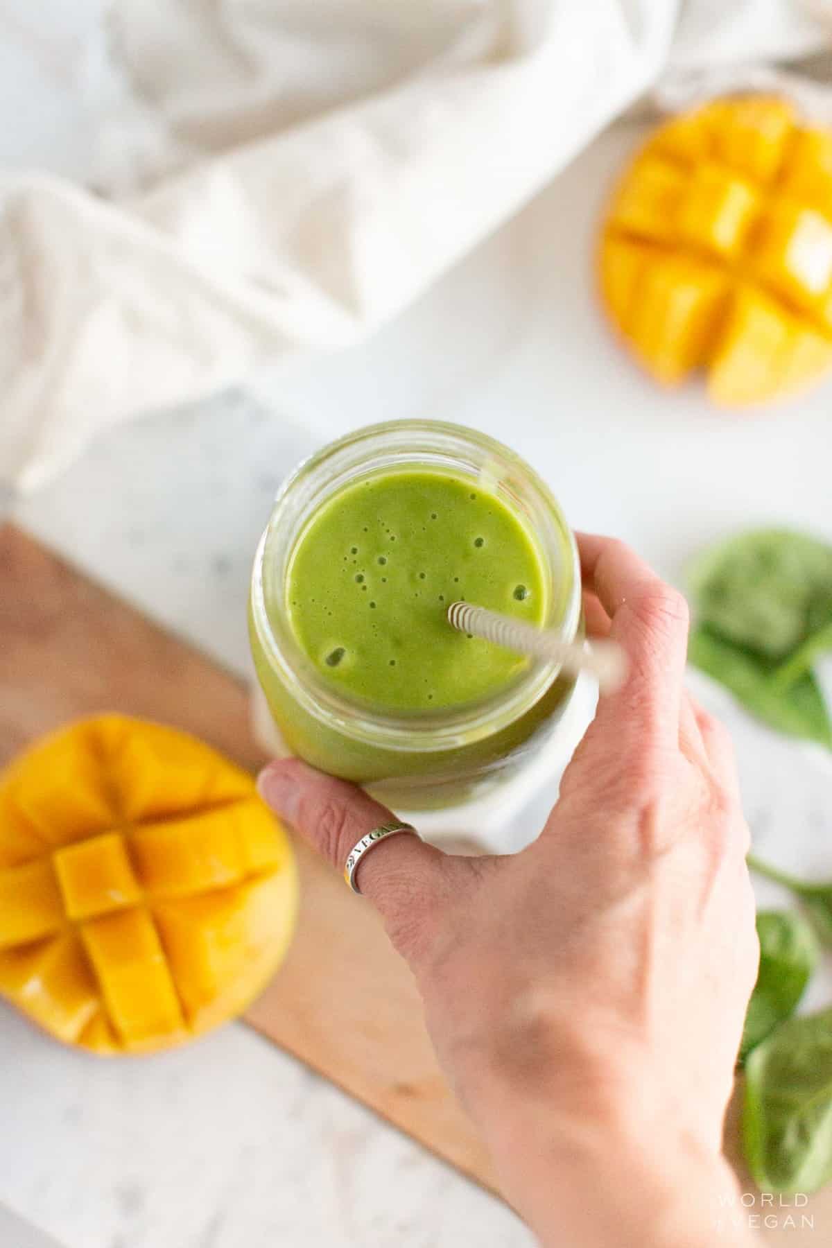 A hand picking up a glass of a mango spinach smoothie.