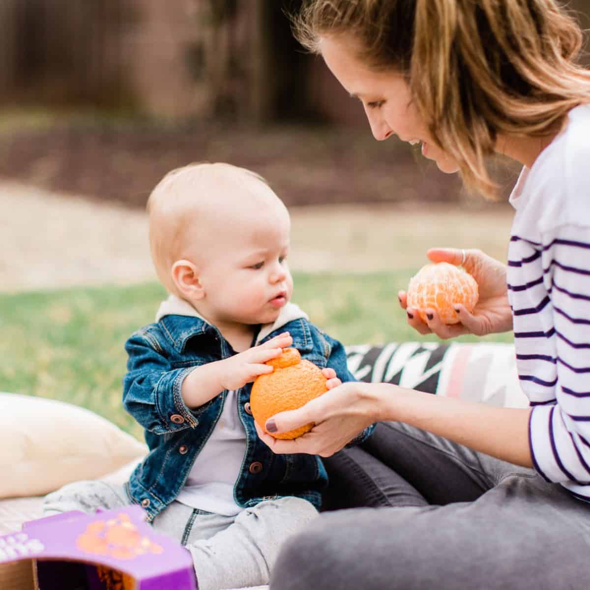 Plant based mom Michelle Cehn holding out a sumo citrus orange as a vegan snack for her kid toddler.