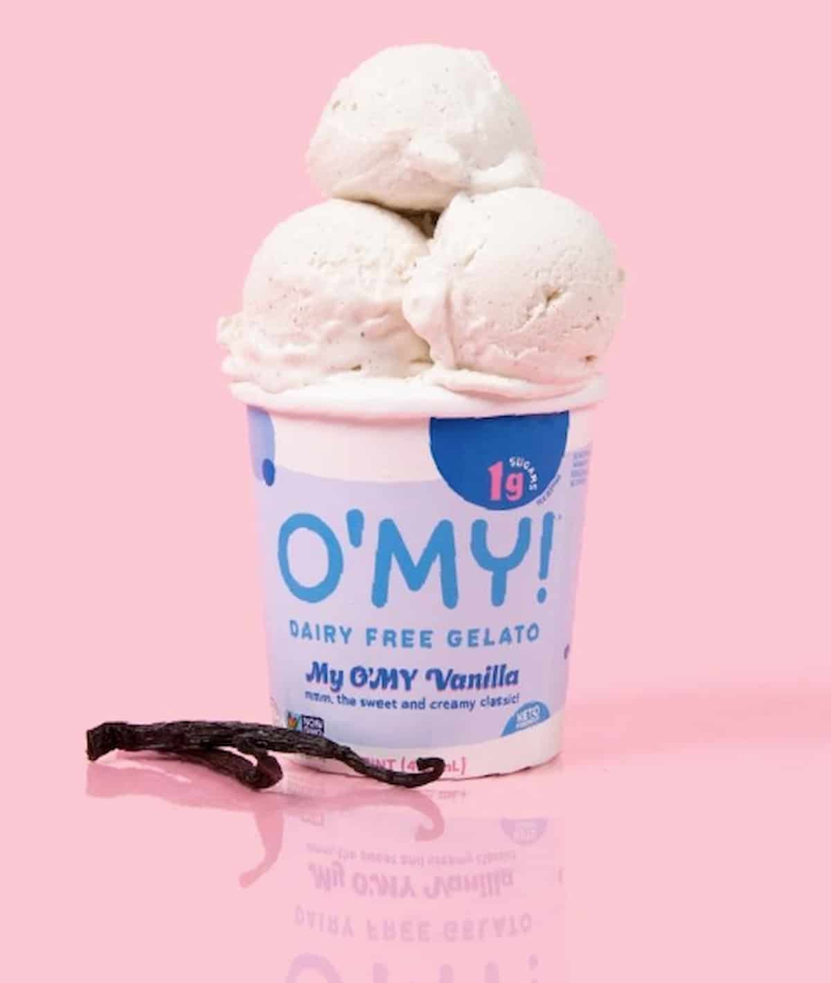 O'My Dairy-Free Gelato pint with three scoops on top and vanilla beans beside it.