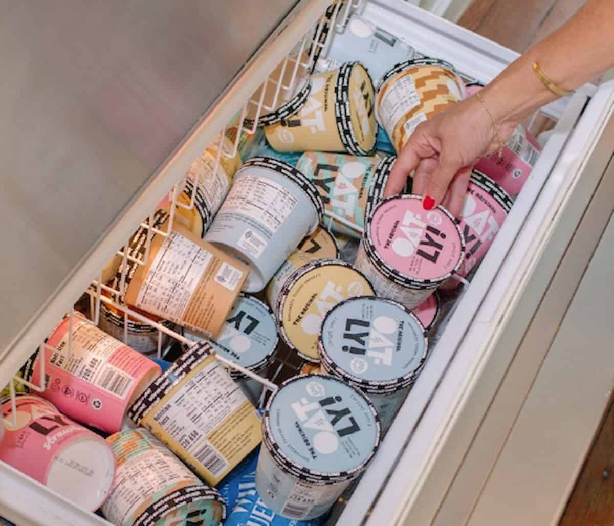 Freezer full of pints of Oatly oat-based ice cream with a hand reaching in to grab one.