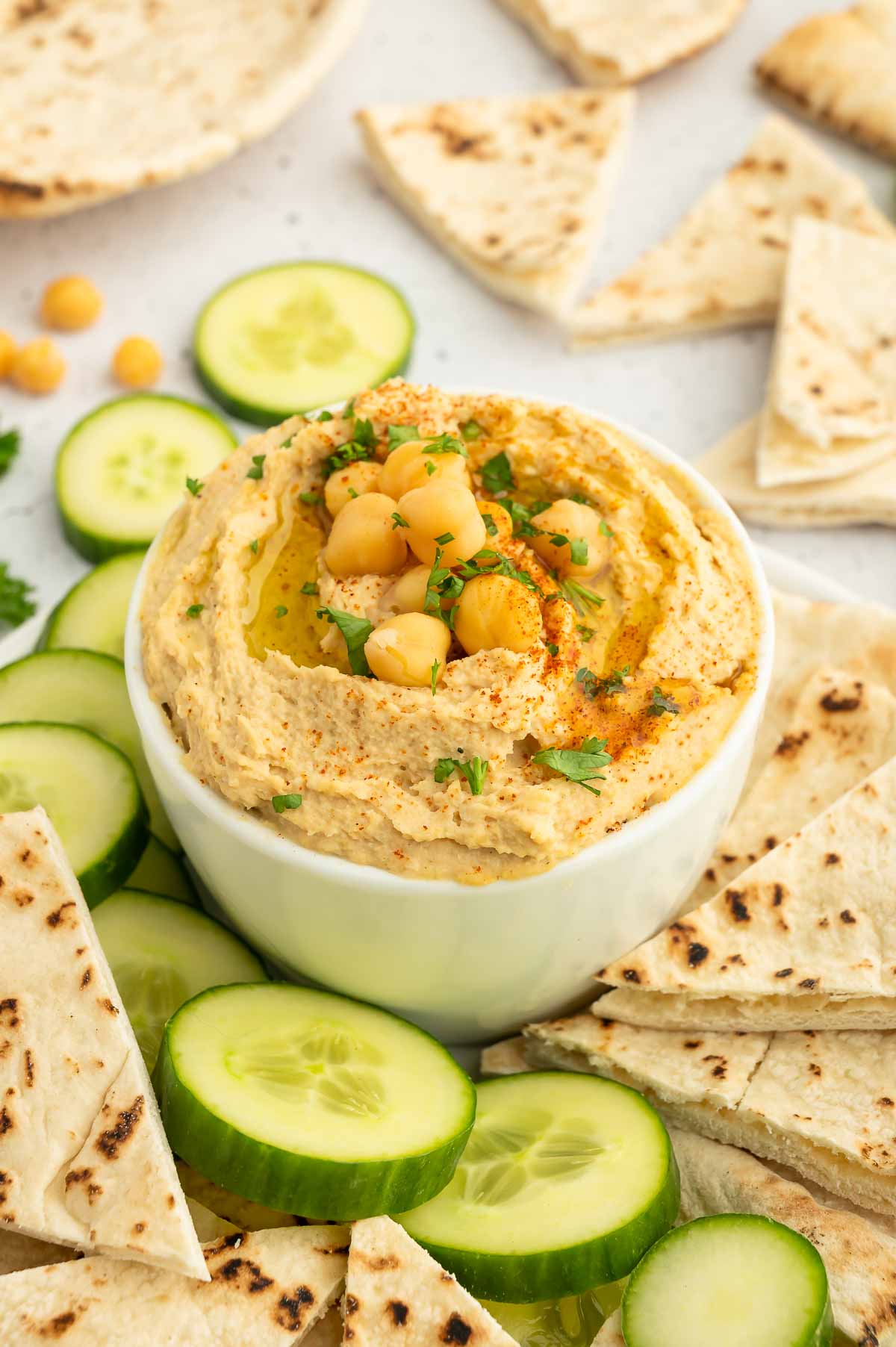 A bowl of hummus with cucumbers and pita.