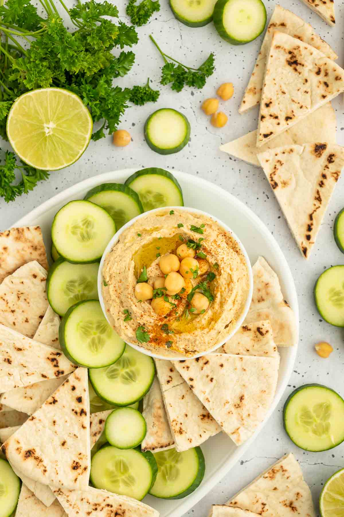 A plate with hummus, pita, and cucumbers.