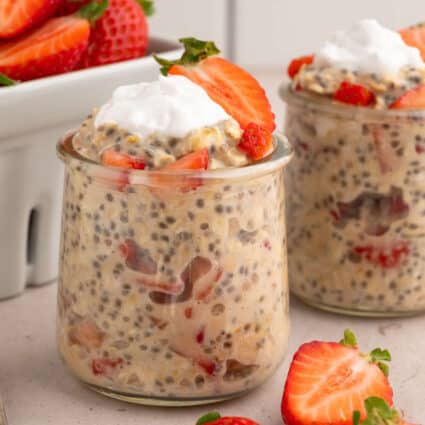 Two glass jars of overnight oats topped with strawberries and coconut whipped cream.