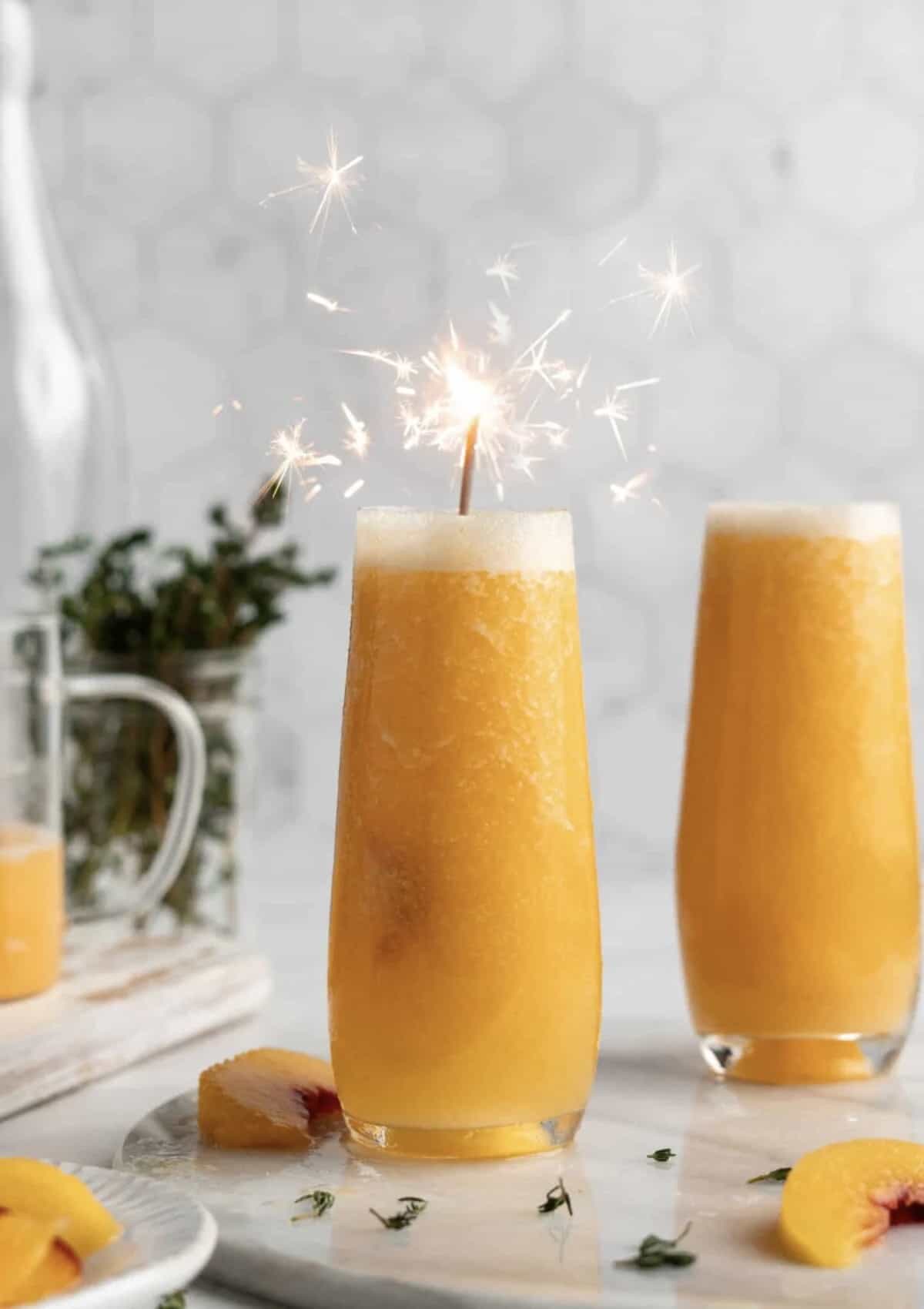 Festive photo of peach bellini cocktails in pretty glasses with a sparkler. 