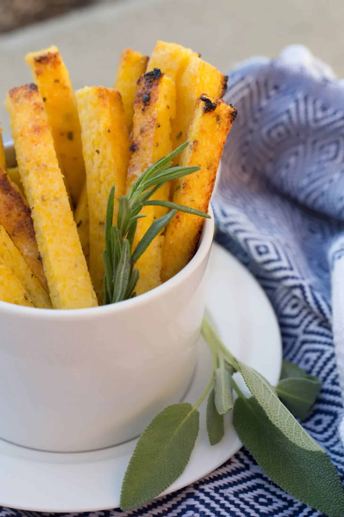 polenta fries with rosemary in a white cup on a white plate with a sage bunch