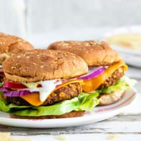 Three tempeh chickpea burgers in buns with toppings on a plate.