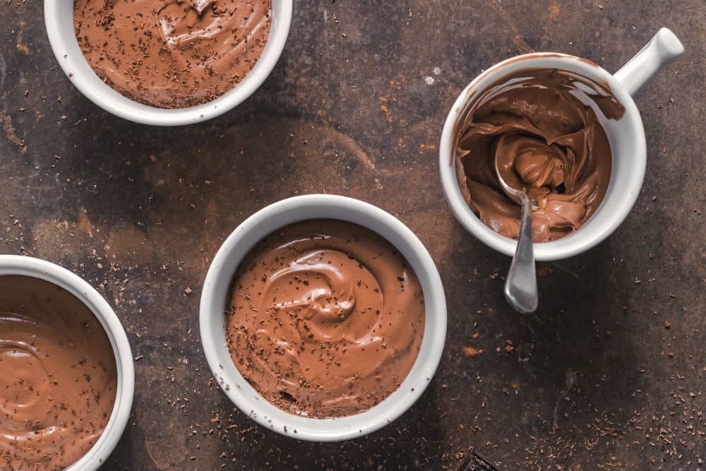 vegan chocolate pudding in multiple mugs against a brown surface