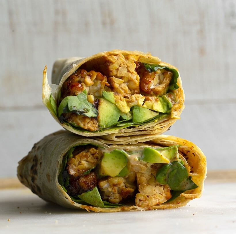 wrapped tortillas stacked on top of each other, filled with avocado, tempeh, and spinach