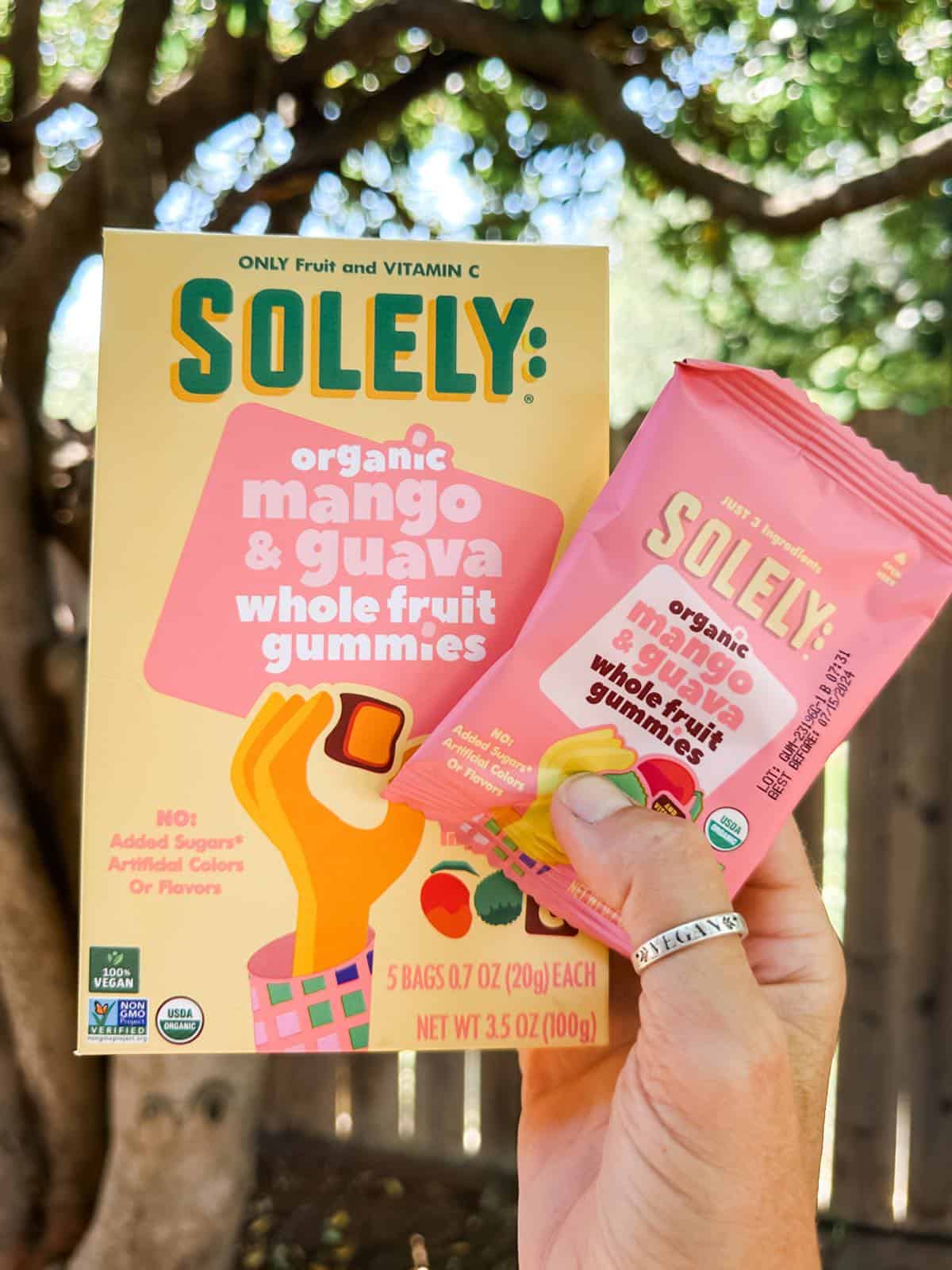 Vegan mom holding out a box of healthy fruit snack chews from the brand Solely, in mango guava flavor. 