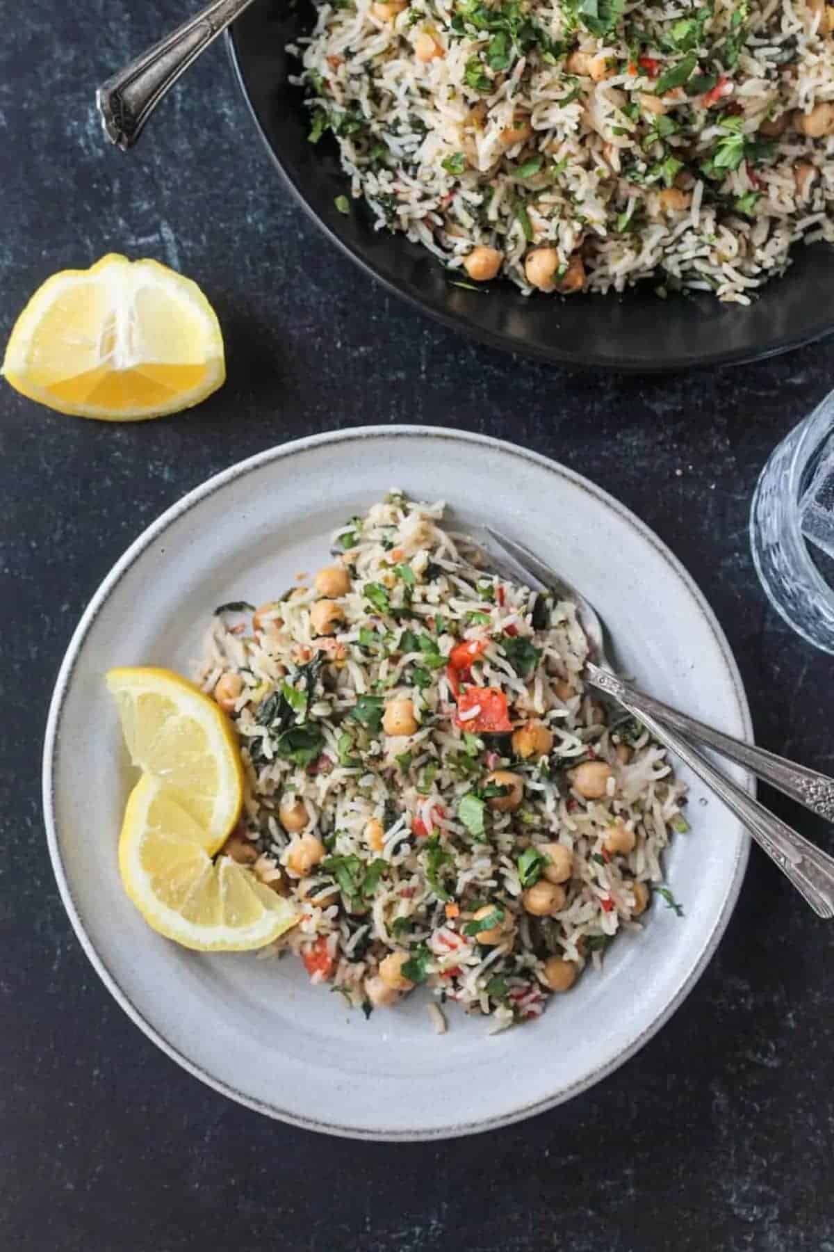 Spinach rice and chickpeas on a plate with a fork and spoon and two lemon slices.