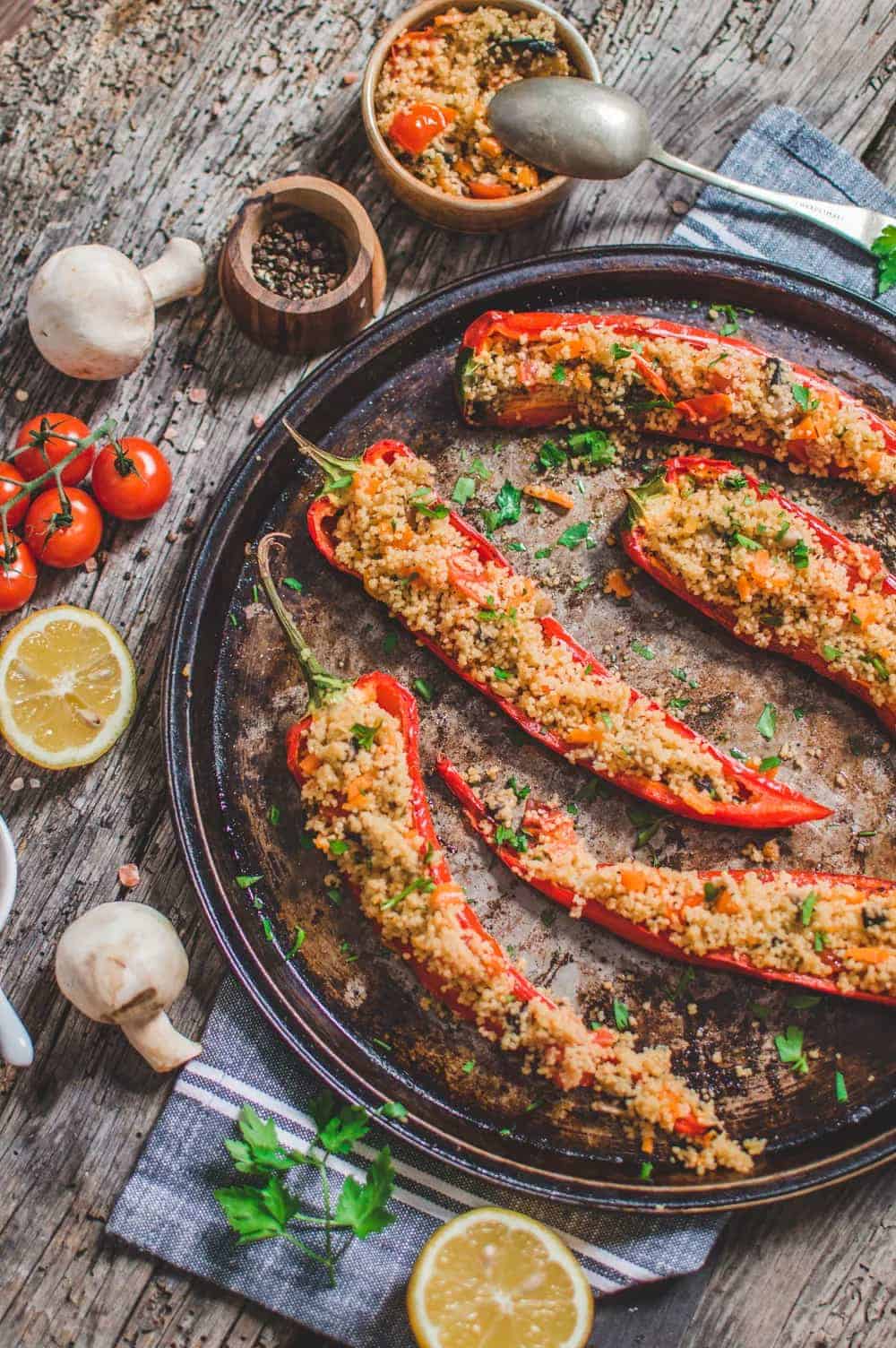 red romano bell peppers stuffed with couscous on a tray surrounded by lemon, garlic, and tomatoes