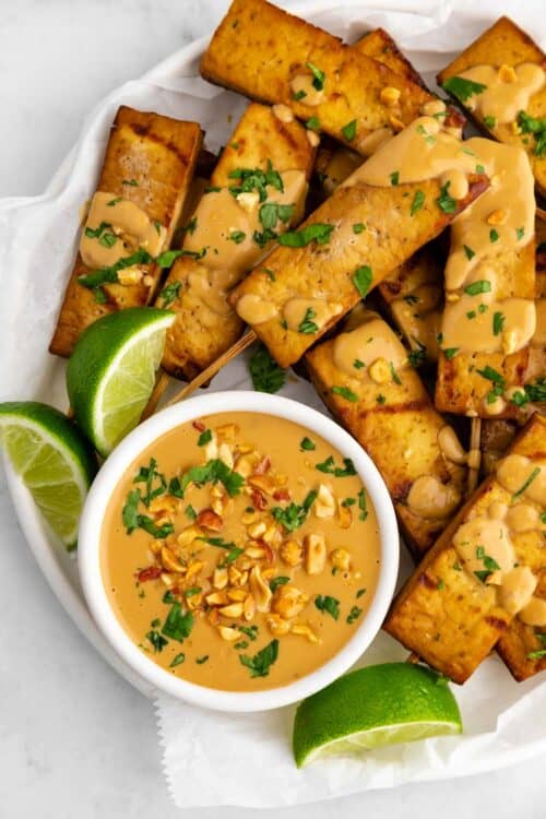 Tofu satay served on a plate with peanut dipping sauce and fresh lime slices.