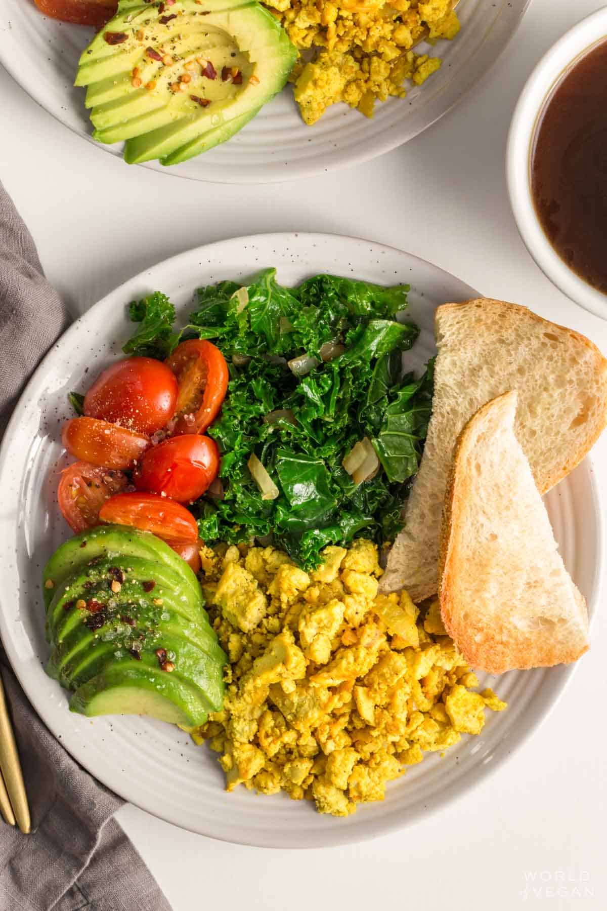 tofu scramble served up on a vegan breakfast plate with avocado tomatoes greens and toast