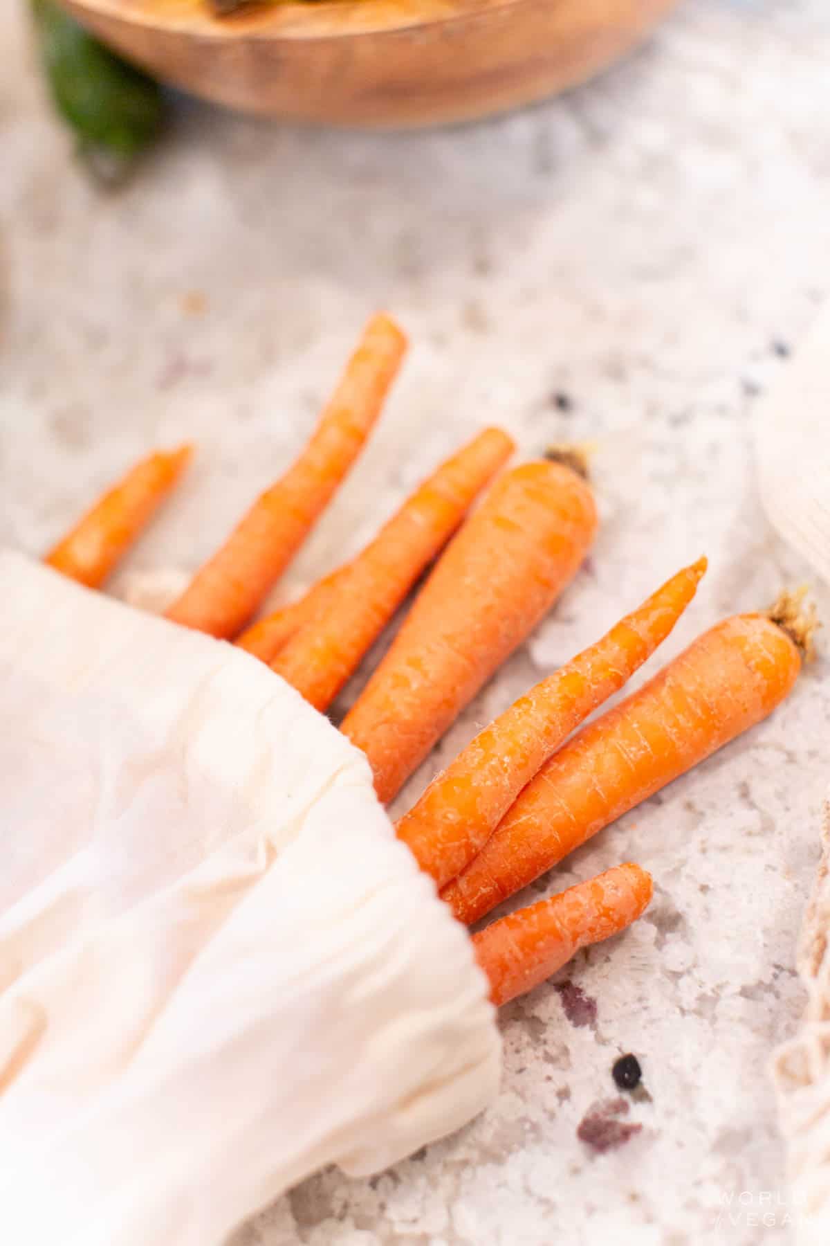 A sack of carrots laying on a countertop with the carrots poking out of the end of the bag.