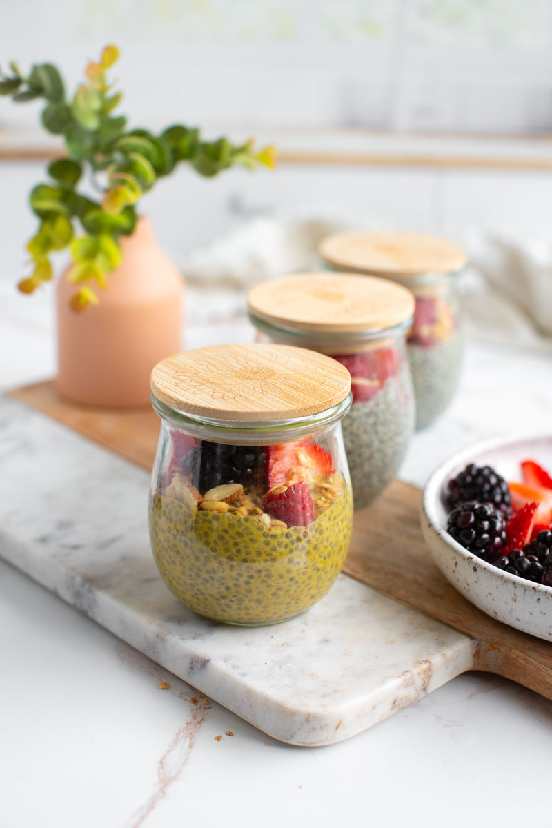 Vanilla chia puddings in small glass jars lined up in a row next to a bowl of berries.