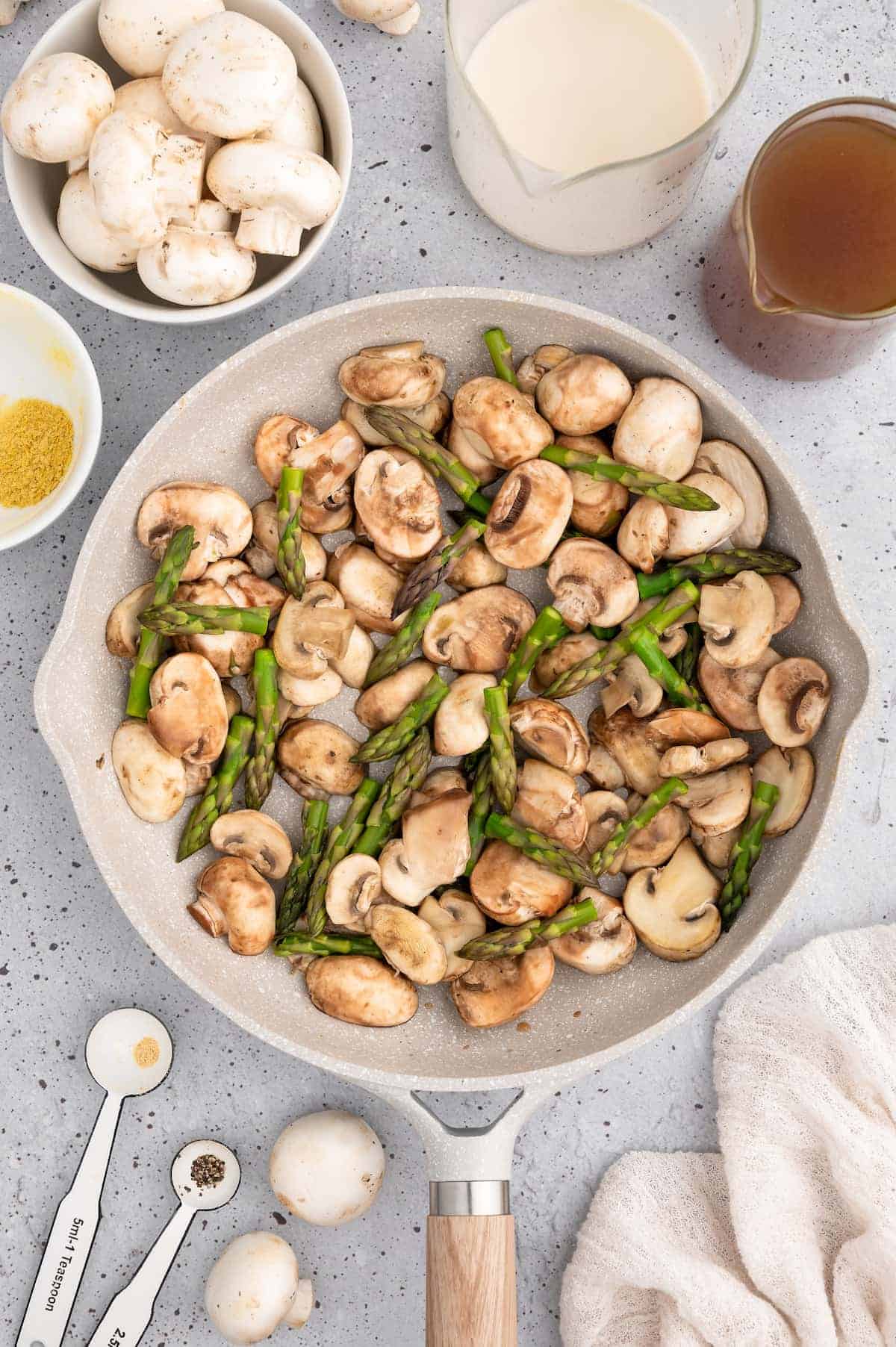 Mushrooms and asparagus sautéeing in pan.