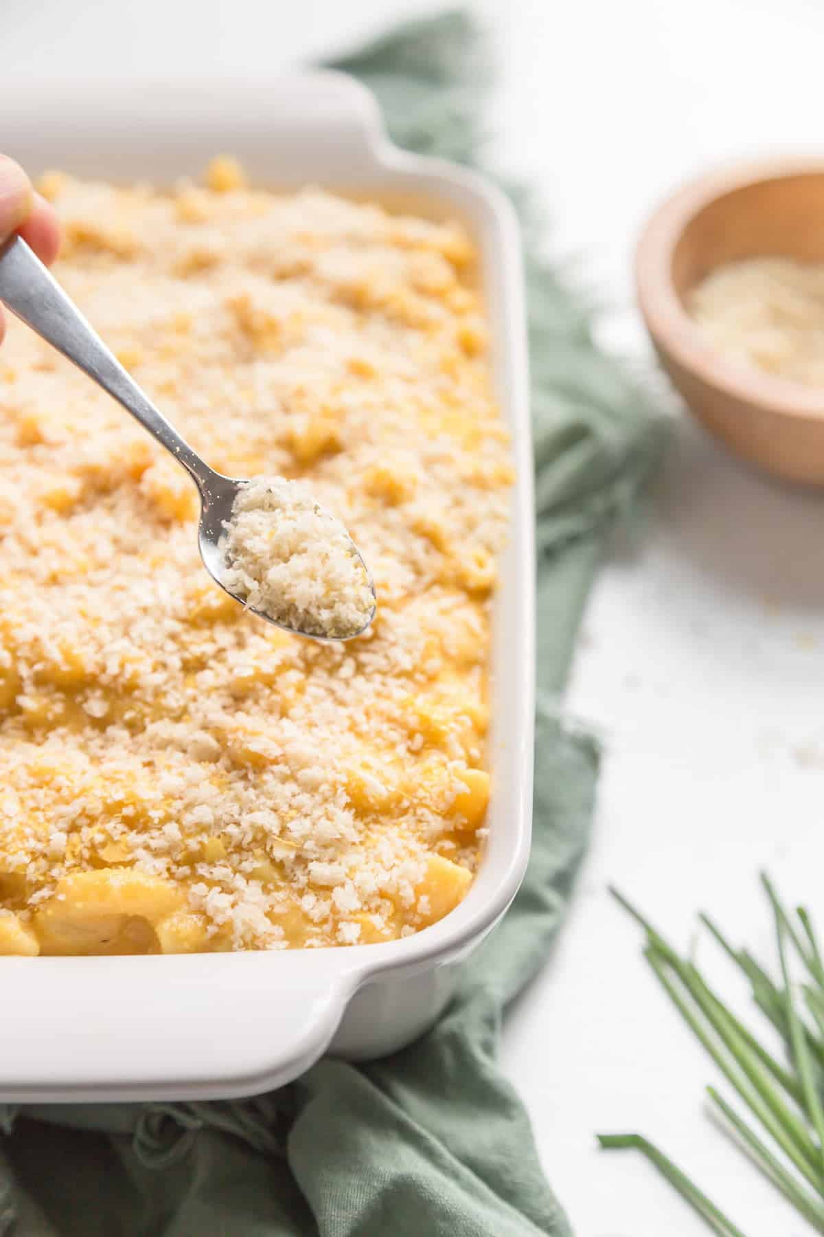 Breadcrumbs being sprinkled onto a vegan mac and cheese in a white casserole dish.