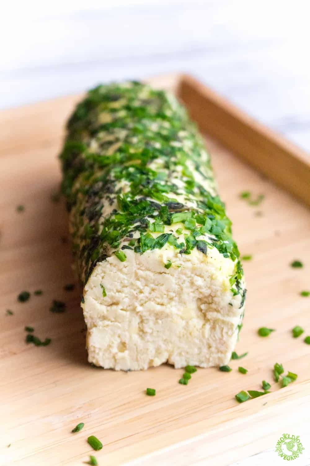 vegan cheese log on a wooden board with chopped chives
