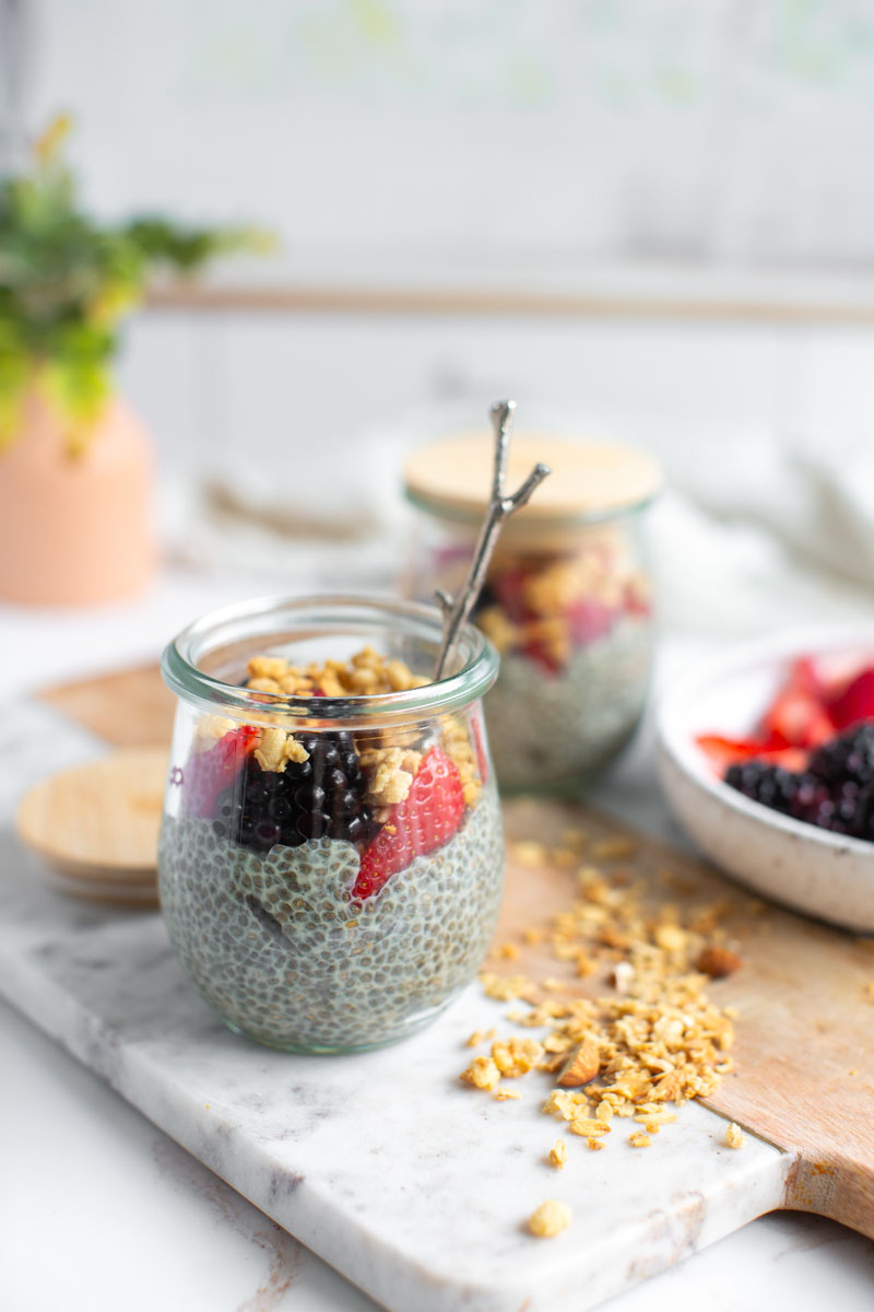 Vegan vanilla chia seed pudding in small jars, topped with berries and chopped nuts.