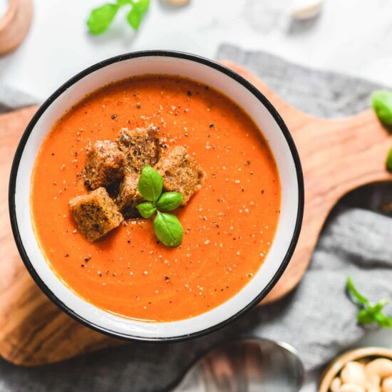 Easy Vegan Creamy Tomato Soup Garnished With Basil and Croutons on a Wood on a Cutting Board