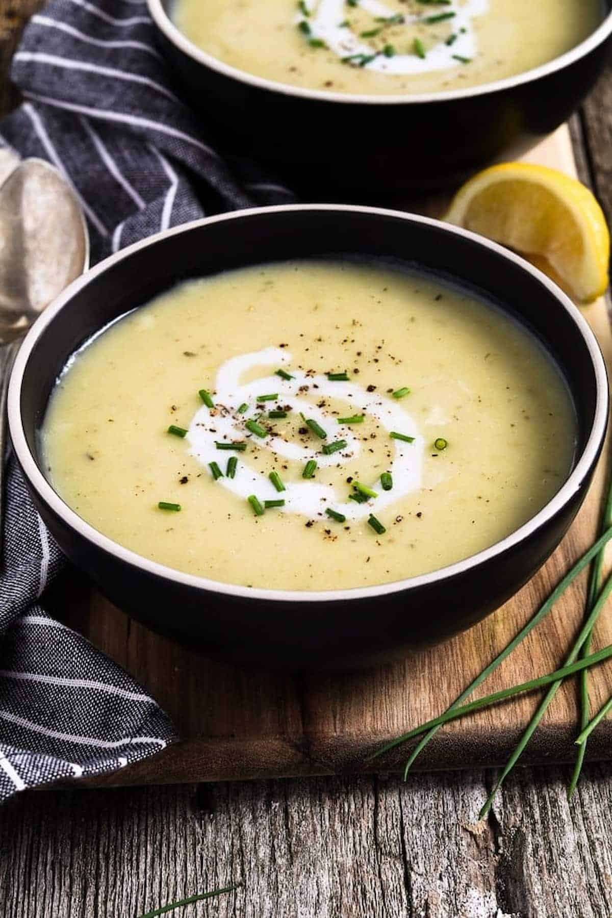 Bowl full of potato leek soup topped with coconut cream swirl and chives.