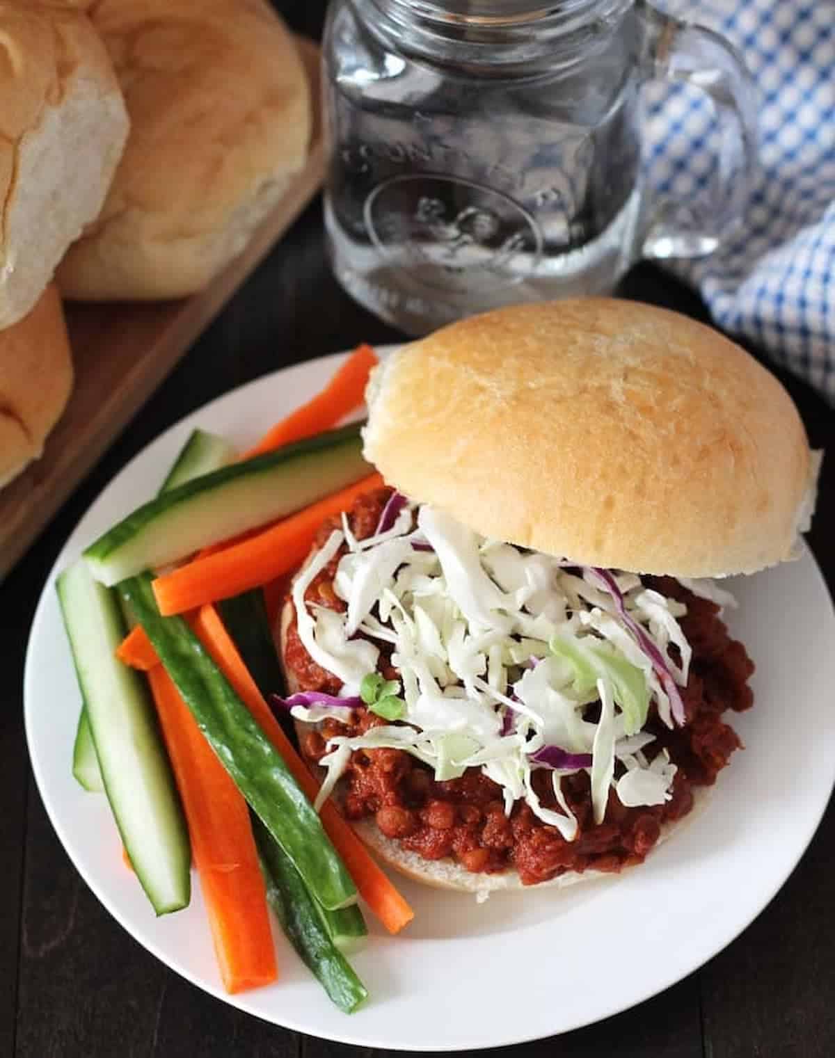 Vegan lentil Sloppy Joes on a bun served with slices of carrots and cucumber.