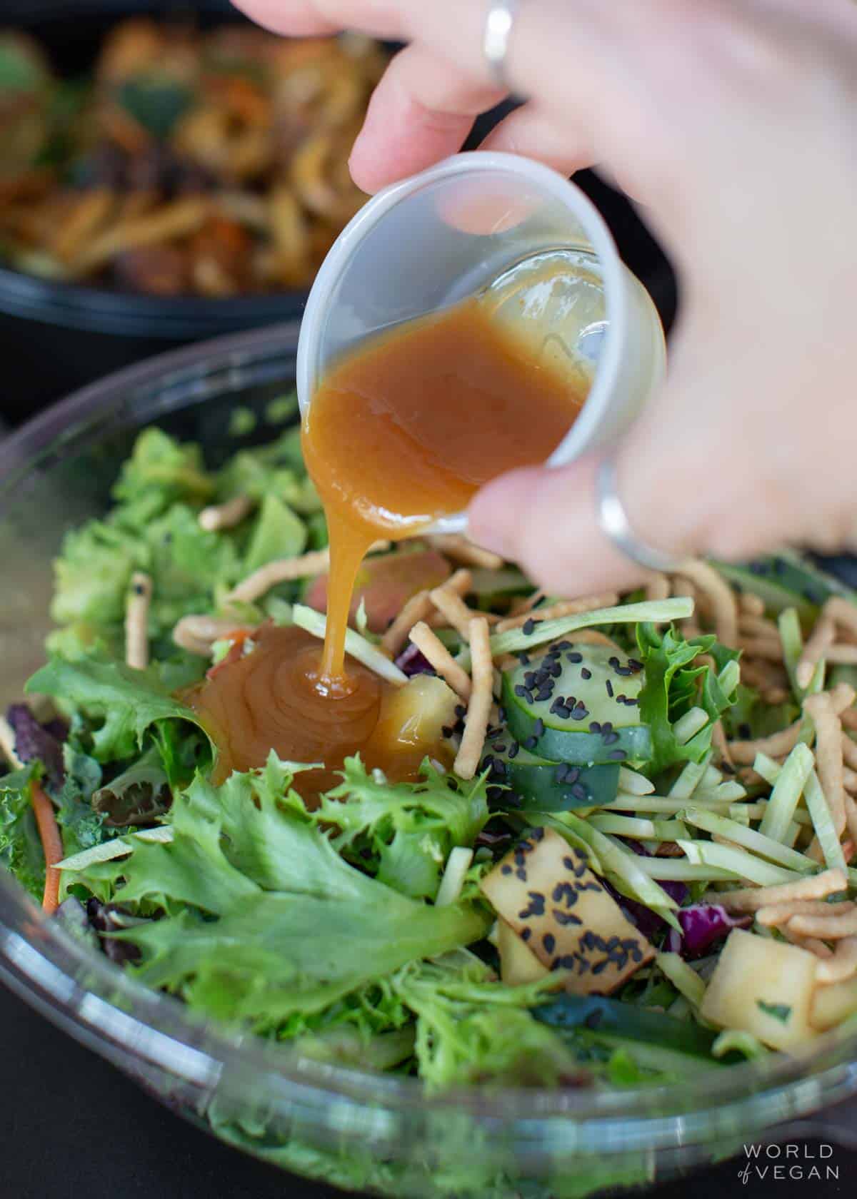 pouring dressing over the vegan asian salad at noodles and company