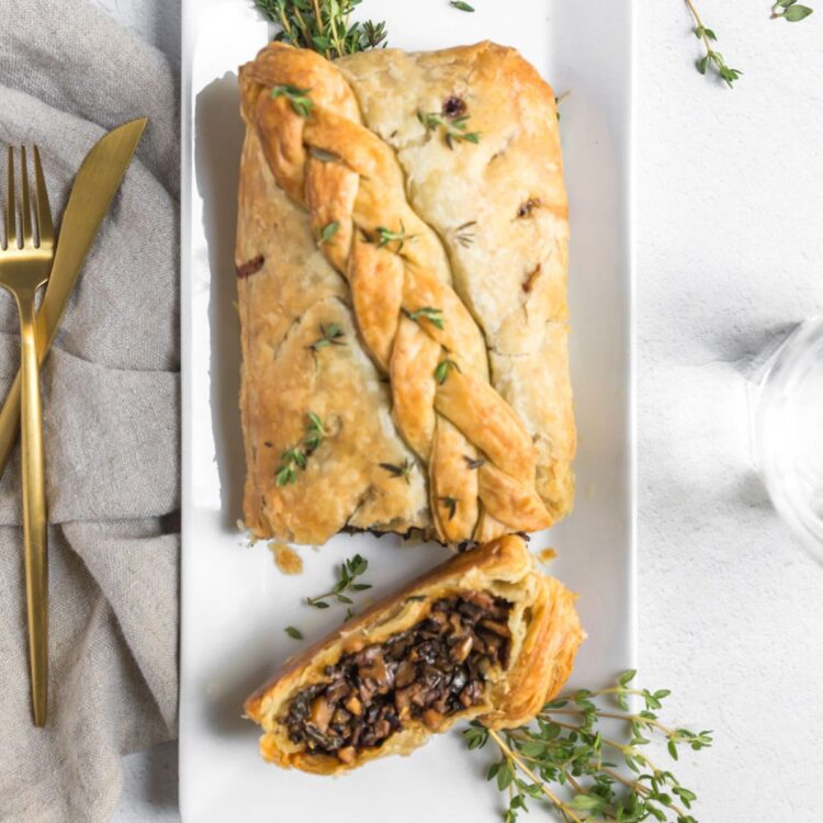 Vegan mushroom wellington on a serving platter with one slice cut off, laying beside the rest of the roast.