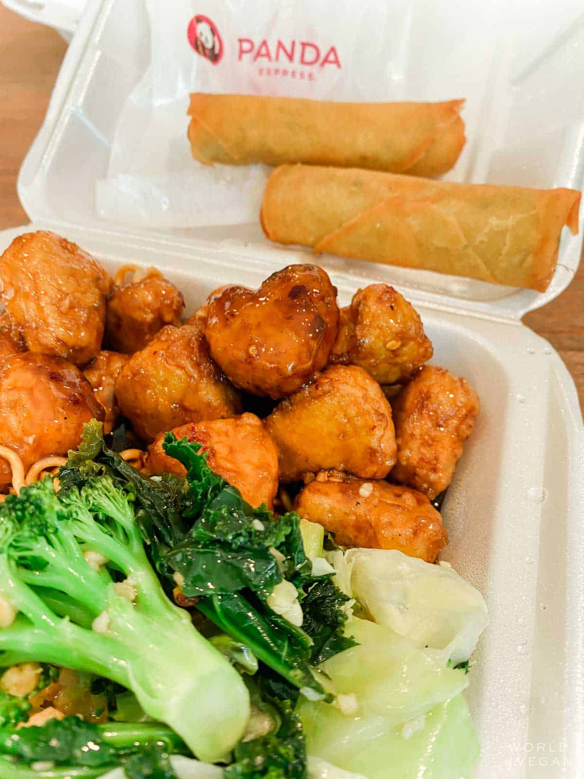 To-go container of vegan Beyond Orange Chicken, spring rolls, and broccoli from panda express. 