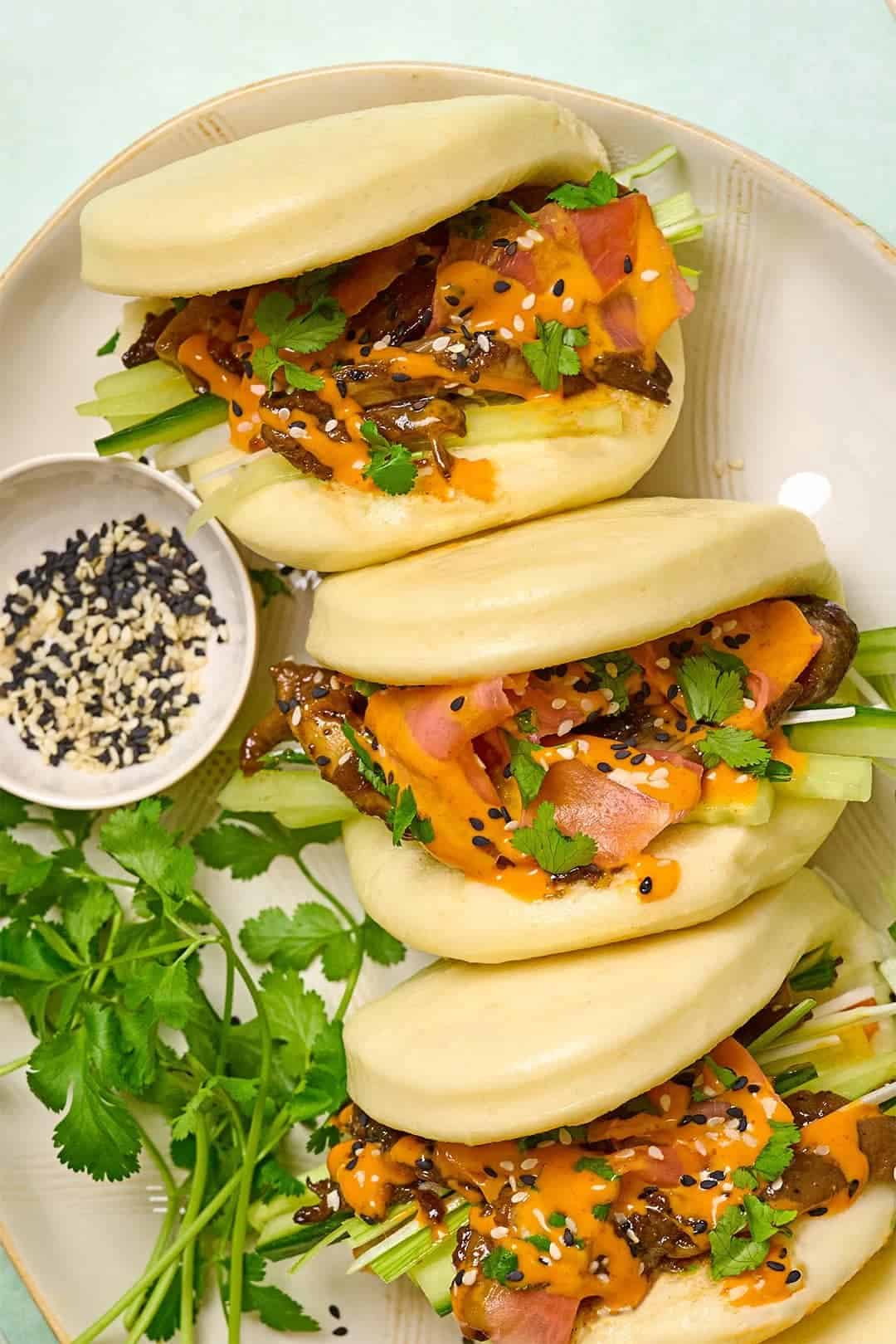 bao buns filled with oyster mushrooms, sliced cucumber, pickled red onions, and vegan spicy mayo garnished with black sesame seeds and cilantro