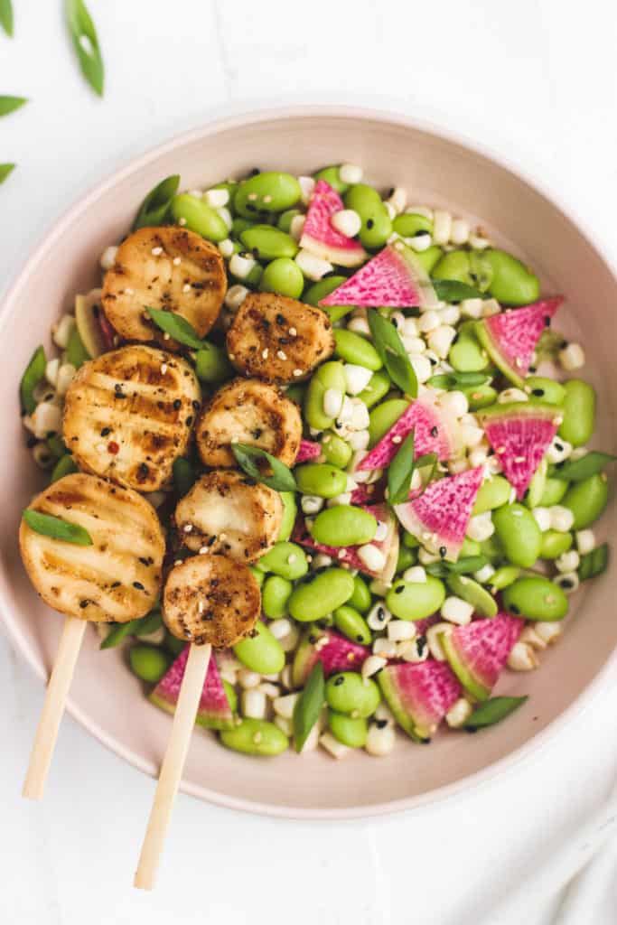 scalloped oyster mushrooms on skewers atop a plate of edamame, corn, and watermelon radishes