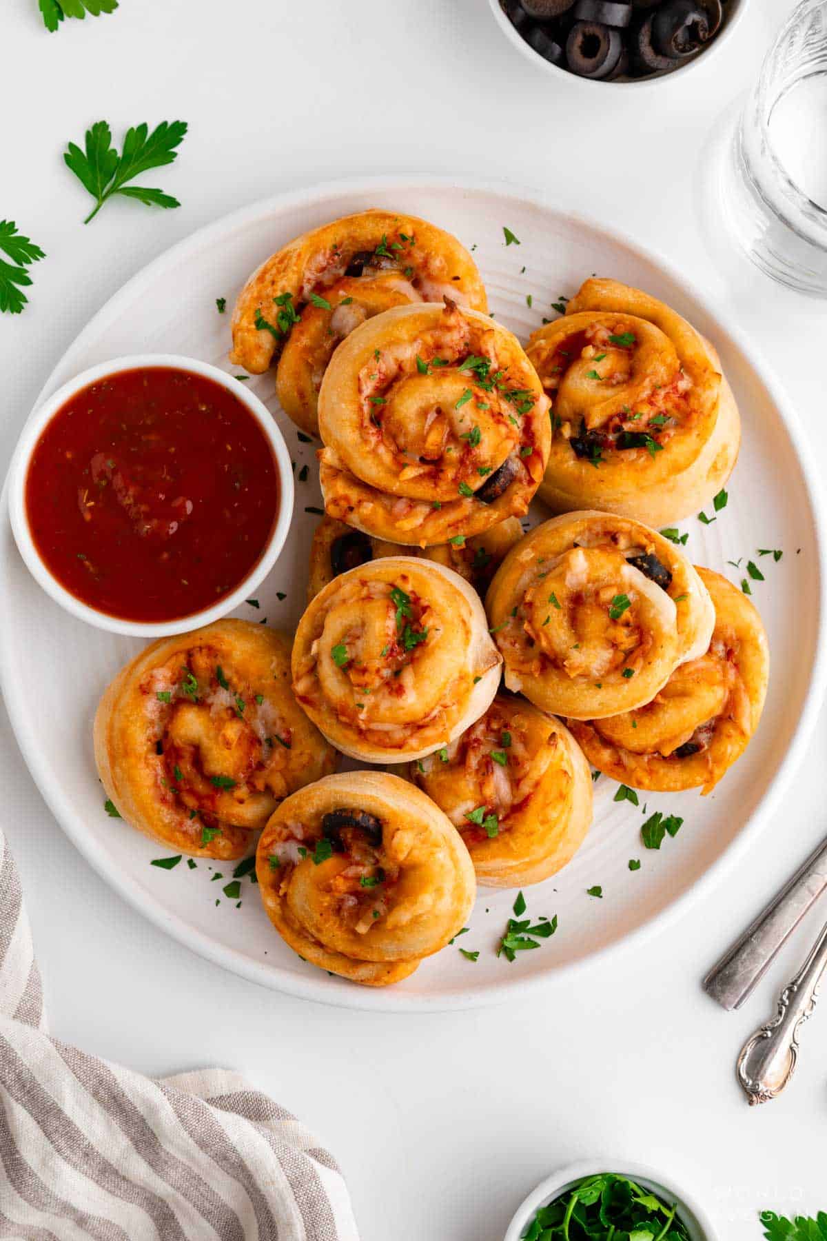 Vegan pizza rolls stacked on a plate with dipping sauce.