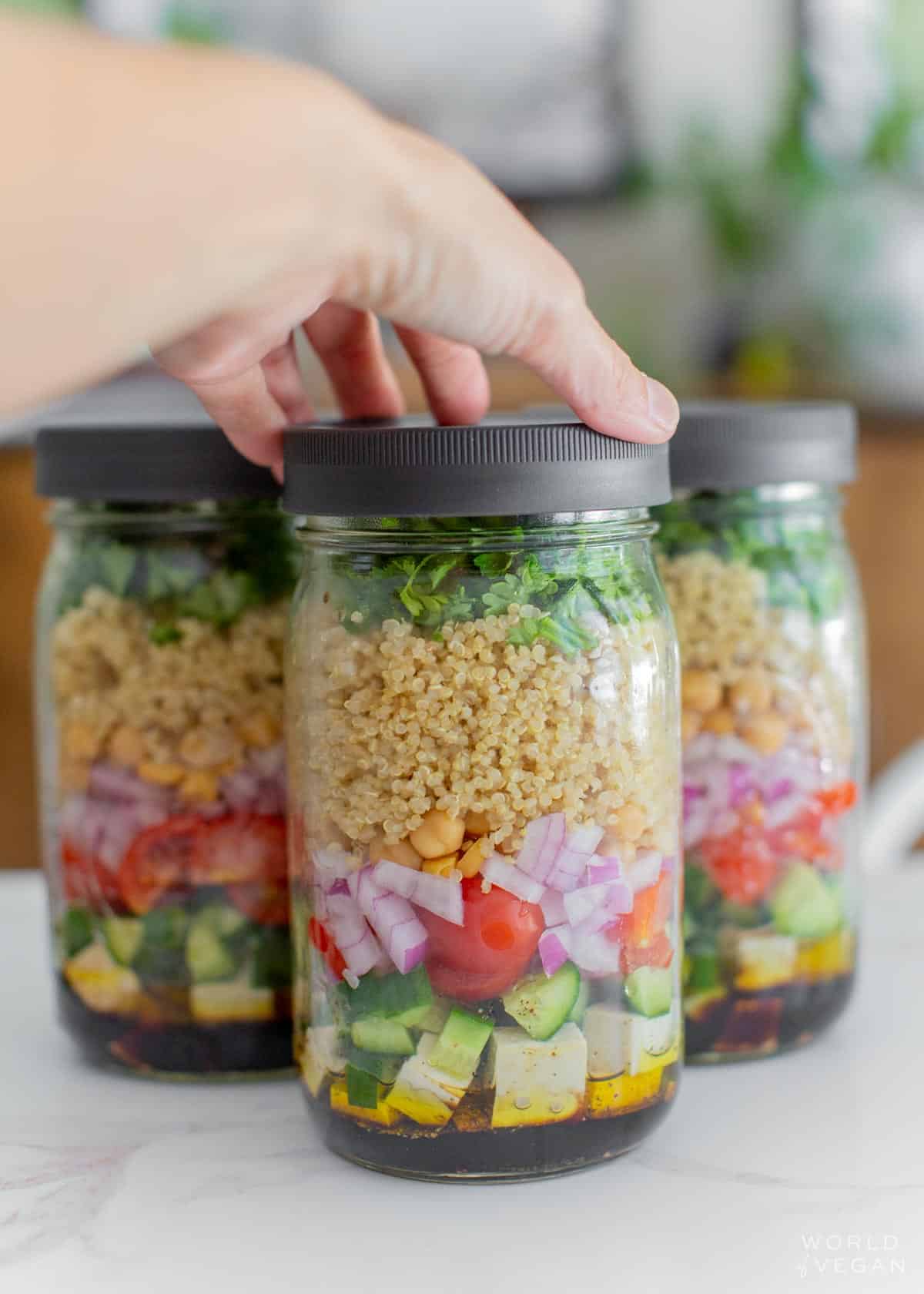 A hand reaching for a jar of vegan quinoa salad.