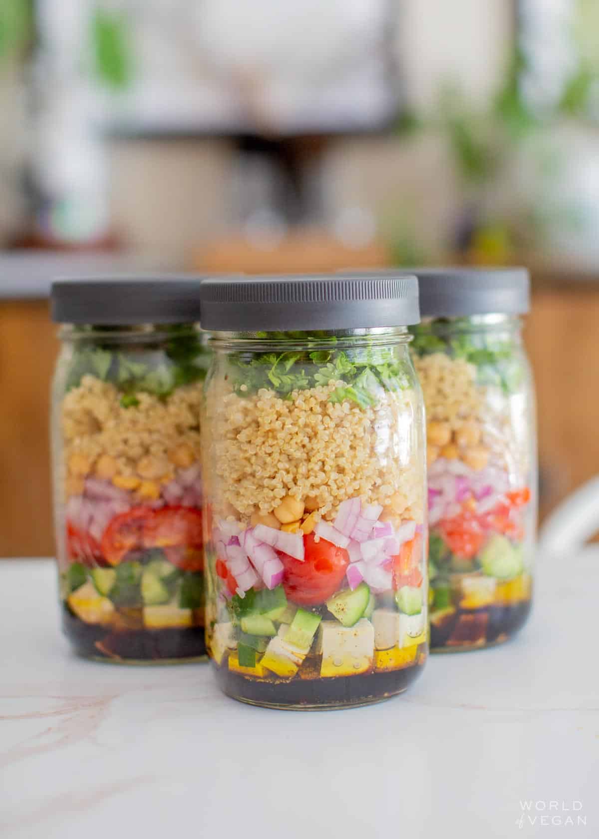 Three large mason jars full of vegan quinoa salad.