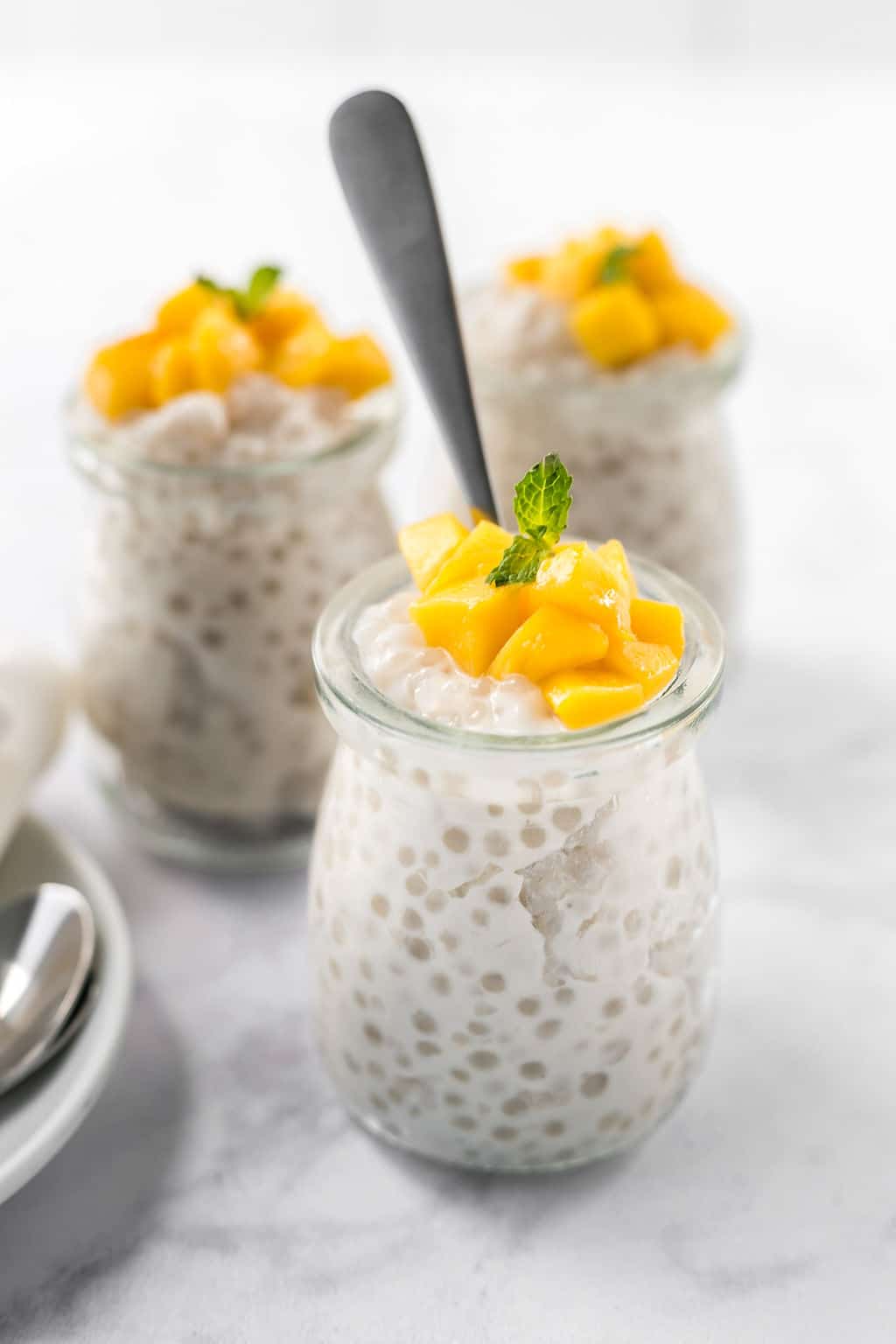 Easy Dairy-Free Tapioca Pudding in small glass jars topped with mango and a sprig of green mint.