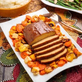 Sliced Plant-Based Seitan Turkey Roast on a serving platter surrounded by roasted veggies.