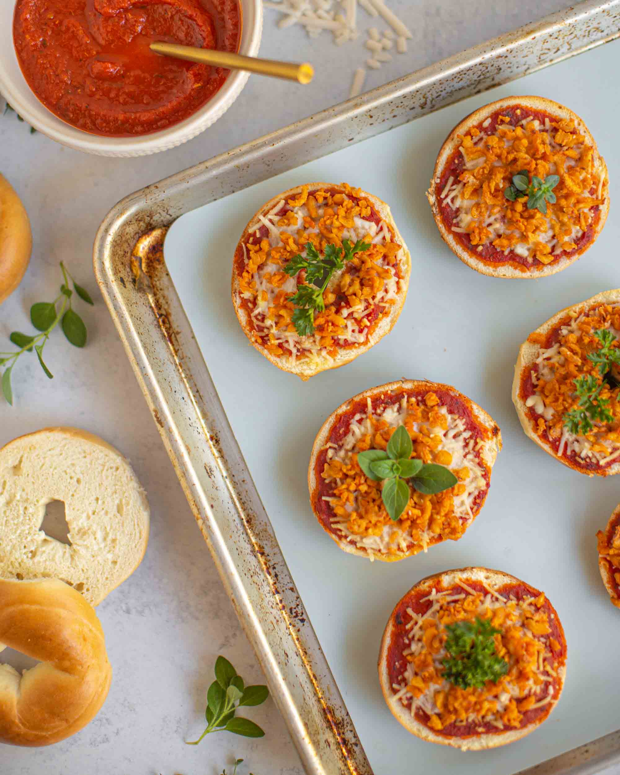 vegan pizza bagels garnished with parsley on a baking sheet. they have tomato sauce, vegan cheese, and vegan beef crumbles